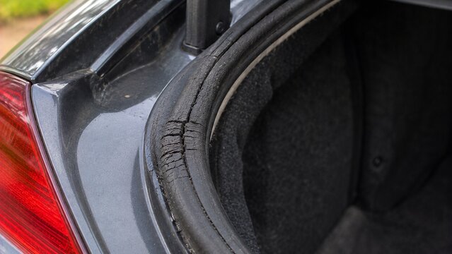 Close-up of vehicle trunk opening showing aging rubber weather seal with visible cracking and compressed damaged section that could allow water intrusion