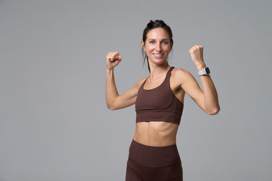 Happy athletic woman flexing muscles and smiling at camera in studio portrait