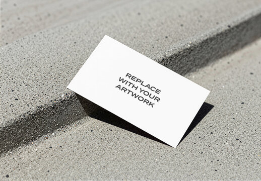 Business card mockup with placeholder text resting on a concrete surface, angled view of stationery branding presentation in an outdoor urban environment, Template