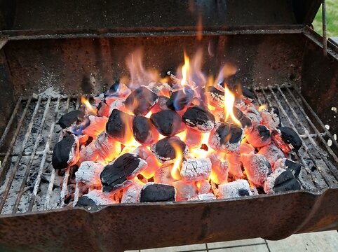 Glowing charcoal briquettes burning with bright orange flames inside an old metal grill. Cooking concept for outdoor backyard summer barbecue parties.