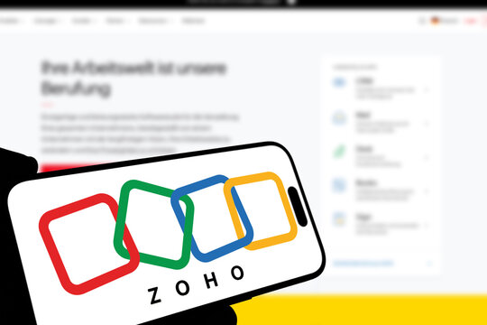 Kiel, Germany - 08-19-2026: Smartphone displaying Indian business software company Zoho logo in front of companys webpage