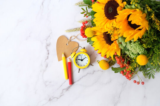 bright bouquet with sunflowers, heart blank card, pencils and alarm clock on marble table background. autumn seasonal composition. symbol of fall time, End of summer, 1 september. flat lay. copy space
