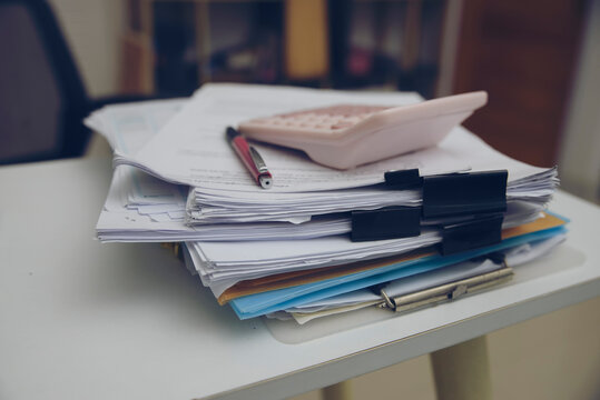 Stack of financial documents with a calculator and pen on a desk, representing tax calculation, accounting, budgeting, financial planning, and paperwork management.