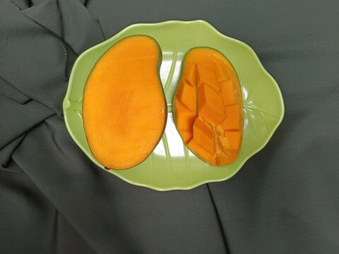 Buah mangga masak diiris jadi 2 di sajikan di piring hijau 