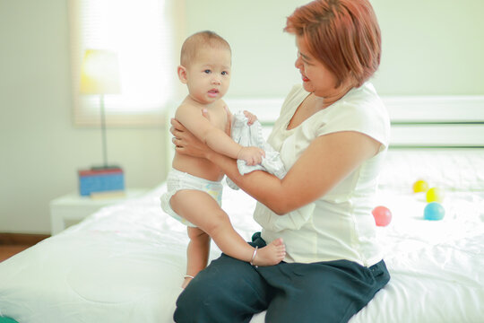 Young mother gently cradles her adorable baby clad only in a diaper in her arms loving smile filling the air in the cozy bedroom of their home becomes precious family memory every day.