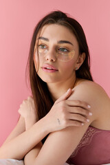 Young beautiful woman relaxing with glittering eye patches against a soft pink background