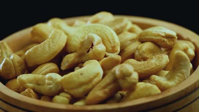 Close-up of roasted cashew nuts slowly rotating in a wooden bowl against a black background. Healthy, organic, and delicious vegan snack.