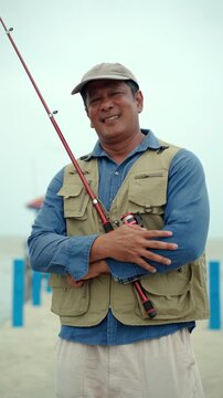 Happy senior man sitting by the sea and fishing with a rod after retirement. Active aging, healthy longevity, outdoor leisure, fulfilling retirement. Life insurance and financial security concept.
