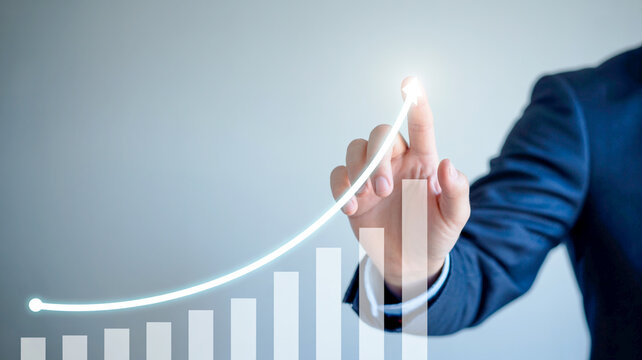 Business professional using a finger to trace a growth chart on a blurred background, symbolizing success and progress in financial markets