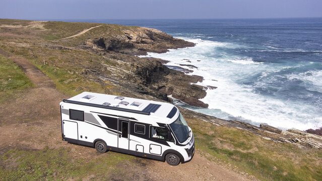 Aerial view of a modern camper van parked on a rugged cliffside overlooking the Atlantic Ocean near the coast of Isla Pancha, Lugo, Spain.