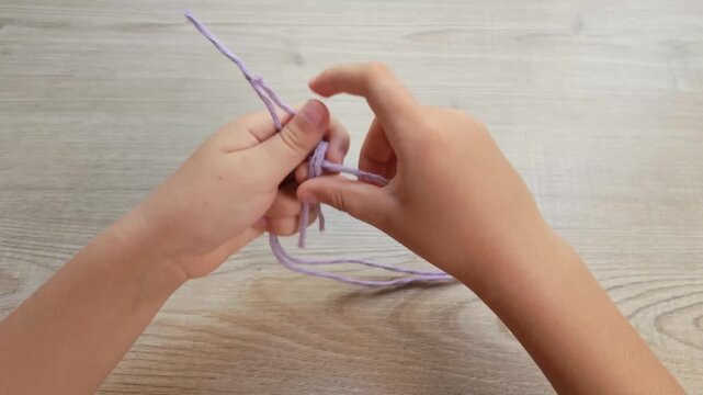 Child Hands Tying a Knot with Purple Rope on Wooden Table