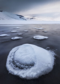 View of snow-covered mounds on the frozen landscape of the Castelluccio plateau with distant mountains under a cloudy sky in Castelluccio, Umbria, Italy.