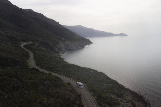 Aerial view of Strada panoramica Alghero-Bosa with a motorhome driving along the winding coastal road surrounded by cliffs and the Mediterranean Sea in Alghero, Sardegna, Italy.
