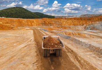 Dump truck hauling gold ore across open pit mine roadway © Parilov