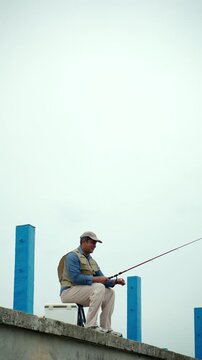 Happy senior man sitting by the sea and fishing with a rod after retirement. Active aging, healthy longevity, outdoor leisure, fulfilling retirement. Life insurance and financial security concept.
