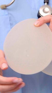 A doctor holding a silicone breast implant close to the camera, demonstrating product details, implant quality, medical device inspection, close up view.