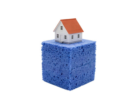 Miniature Residential House Model Resting Atop A Large Blue Porous Cleaning Sponge Representing Home Maintenance And Real Estate Insulation Concept