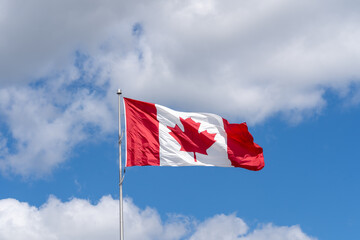 Fototapeta premium A National Flag of Canada waving against a blue sky with white clouds. 