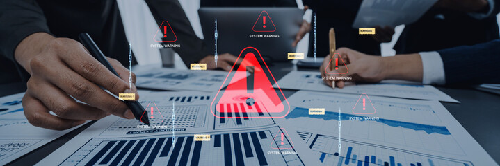 Hands of business professionals analyzing financial charts with warning symbols indicating system hazards during an urgent meeting for risk management and strategy. Glyphic.