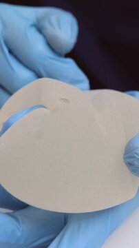 A doctor wearing blue surgical gloves tests the elasticity and softness of a silicone breast implant medical office, plastic surgery procedure, healthcare marketing, clinical consultation