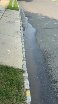 Vertical view of water running down a street near a curb and driveway