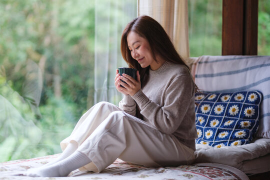 Portrait image of a woman drinking coffee while sitting on a bed at home