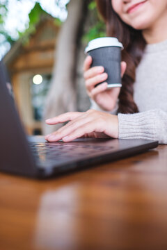 Vertical closeup image of a woman working on laptop computer and drinking coffee in cafe