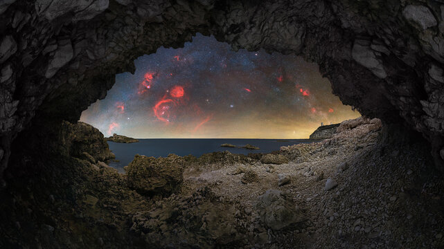 View of the rocky coastline and sea at Capo Mannu seen from inside a natural cave under a starry night sky in Sassari, Sardinia, Italy.
