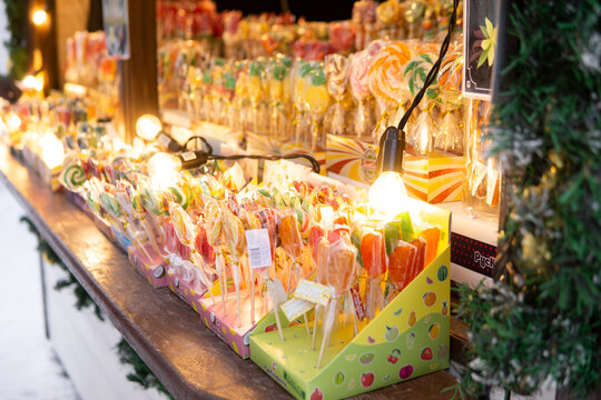 Colorful candy stall displaying lollipops and sweets with glowing lights at a festive market. Seasonal confectionery display for celebration, shopping, and holiday background.