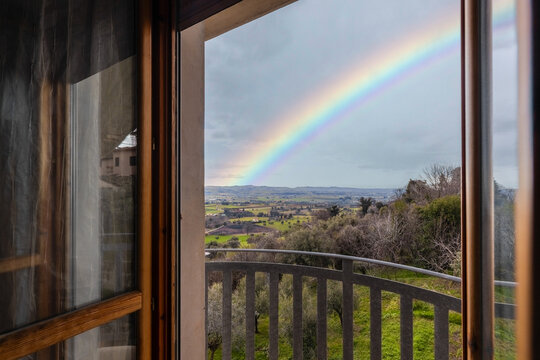 View of a vibrant rainbow arching over the rolling hills and green fields of the Marche countryside as seen from a balcony in Porto Sant'Elpidio, Marche, Italy.