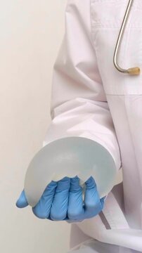 A healthcare provider in blue gloves holds a breast implant in a medical office, plastic surgery and aesthetic medicine healthcare services, professional patient consultation.