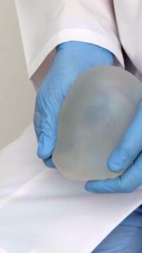 A medical specialist in blue gloves displays a shaped breast implant in a clinic setting, plastic surgery and aesthetic medicine promotion, healthcare consultation and patient care.
