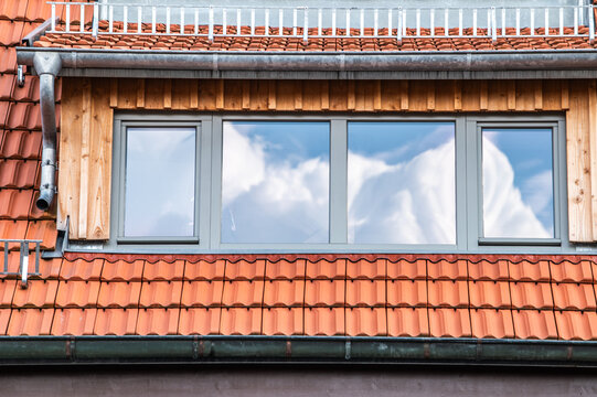 Wei&szlig;e Wolkengebilde vor blauem Himmel spiegeln sich in Fensterfront an Dachgeschosswohnung mit Ziegeldach mit Regenrinne, Regenfallrohr und Schneefanggitter in Neckartenzlingen