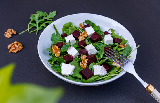 Fresh salad with diced beetroot, feta cheese, arugula and walnuts in white bowl on dark background, keto diet and healthy organic food concept