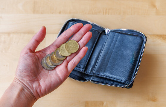 Close up of hand holding Euro coins with open leather wallet on wooden table, personal finance, inflation and budget concept