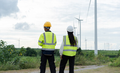 Wind energy engineers overlooking a large wind farm with turbines across a green landscape, representing renewable electricity, sustainability, clean technology and future energy development. © Father_Studio