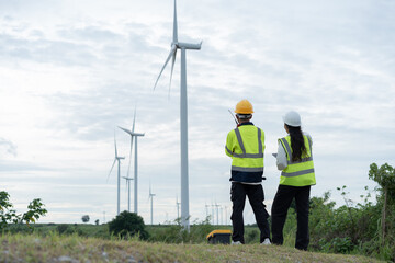 Renewable energy engineers overlooking wind turbines across a rural landscape, representing wind power infrastructure, clean electricity, sustainability and the global transition to green energy. © Father_Studio