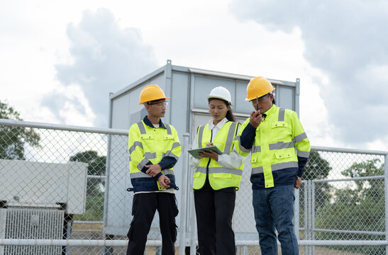 Renewable energy engineering team using a tablet and radio during an outdoor site inspection, representing wind power maintenance, safety management, teamwork and technical field operations.