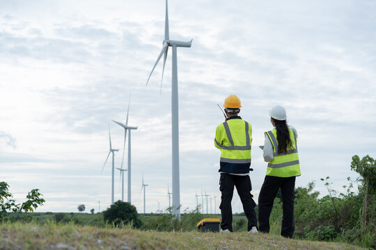 Renewable energy engineers overlooking wind turbines across a rural landscape, representing wind power infrastructure, clean electricity, sustainability and the global transition to green energy.