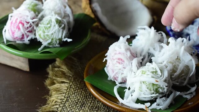 Close-up video of hands sprinkling fresh grated coconut on traditional Thai sweet rice flour dumpling balls served on green banana leaf and rustic plate.