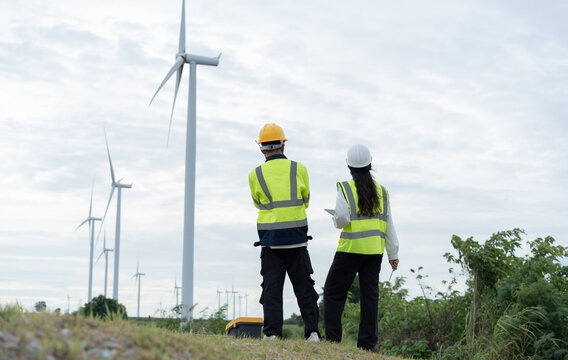 Wind energy engineers in safety gear overlooking turbines at a renewable power site, representing clean electricity, sustainable engineering, inspection and green energy development.