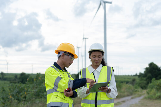 Wind energy engineers reviewing inspection data on a tablet at a wind farm, combining teamwork, digital technology, field maintenance, safety and renewable power operations.