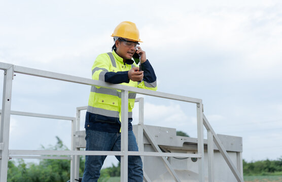 Wind energy technician using a smartphone and radio during field maintenance, representing technical communication, remote support, safety, renewable power service and industrial operations.