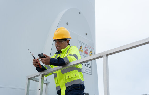 Wind turbine maintenance technician checking a smartphone while holding a radio, representing digital field service, technical communication, safety monitoring and renewable energy operations.