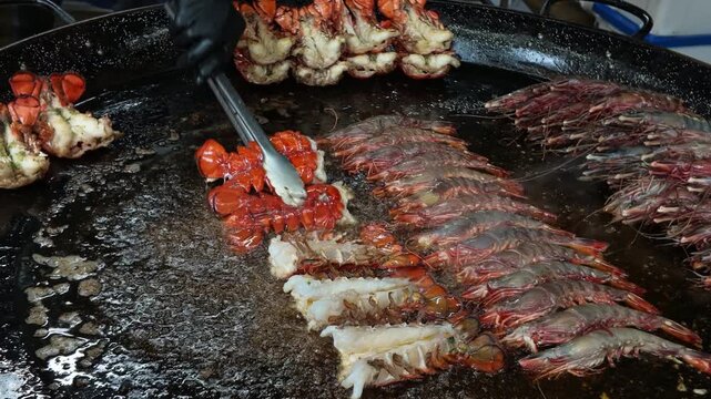 Chef cooking lobster tails and prawns on a large griddle. Street Food