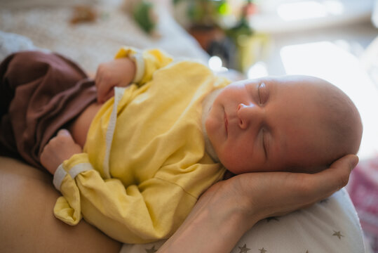 Newborn baby sleeping soundly on adult hands, symbolizing the intimate bond of parental care, security, and love between a mother and her infant in a warm, comforting environment