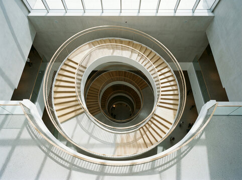 Bird eye view of a wooden spiral staircase lit by an overhead skylight