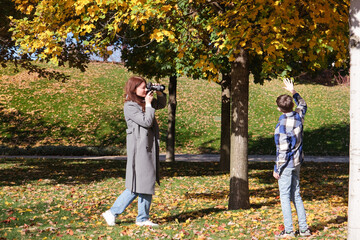 Fototapeta premium adult woman taking pictures of son in autumn leaves in the park or forest