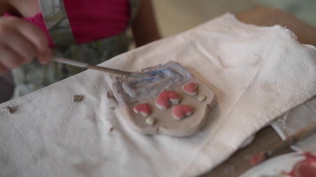 Master class. Children pottery. A view of small children's hands painting a ceramic craft at a table. A girl paints a clay craft using tools, enjoying crafts in a creative workshop. Artistic childhood