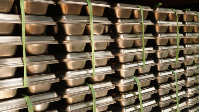 Rows of stainless steel compartment food trays bound together by green raffia rope inside a shelf storage.